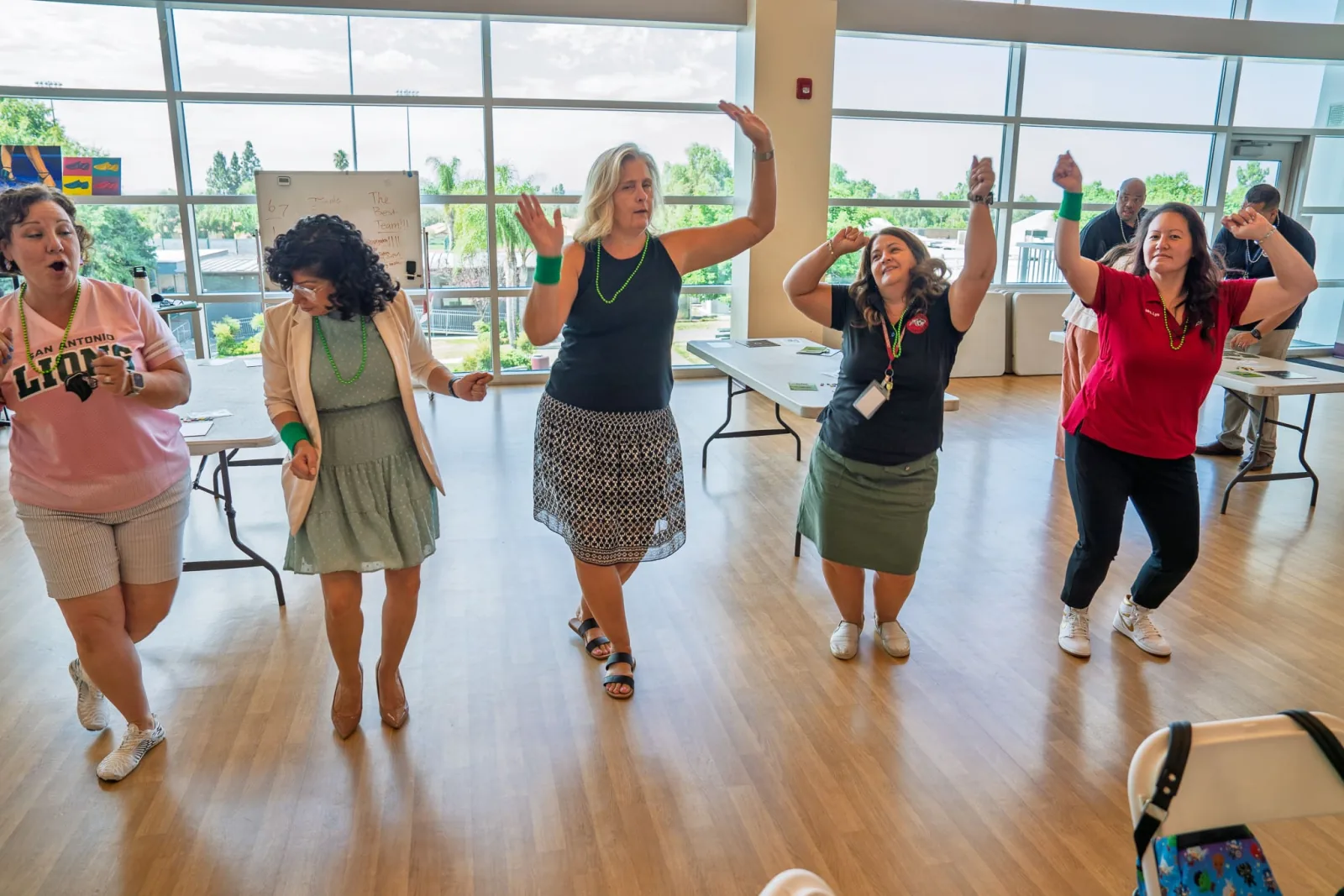 Five colleagues dance with arms raised in a bright, sunlit room